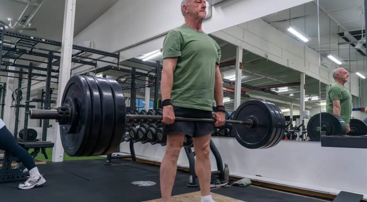 Older man completes a heavy deadlift with wrist straps at Catalyst Training Co. gym in Randwick.