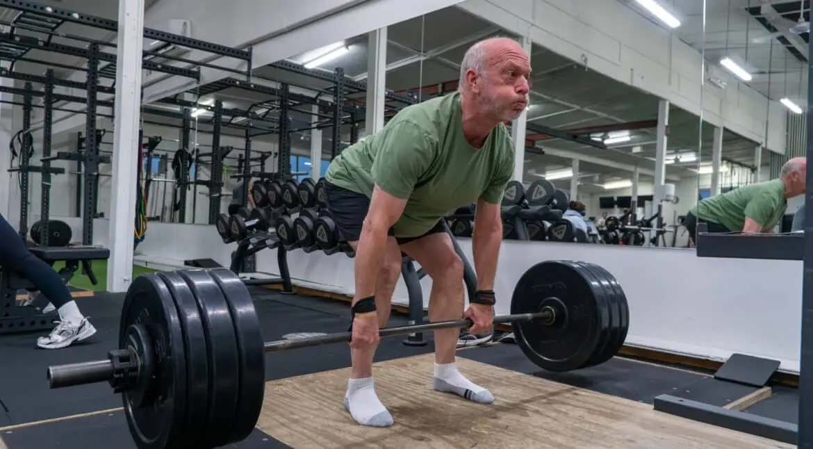 Older man performing a heavy deadlift with a barbell and wrist straps on a lifting platform at Catalyst Training Co. gym in Randwick.