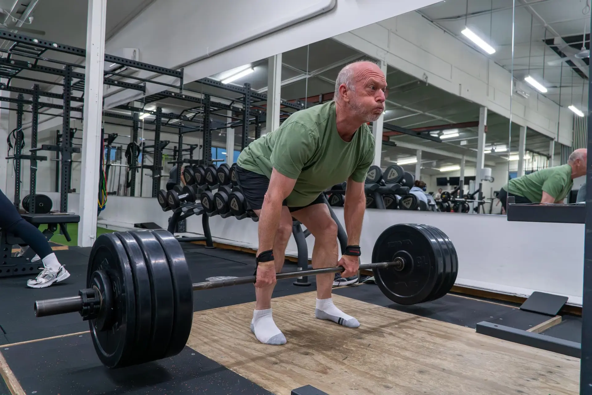 Older man performing a heavy deadlift with a barbell and wrist straps on a lifting platform at Catalyst Training Co. gym in Randwick.