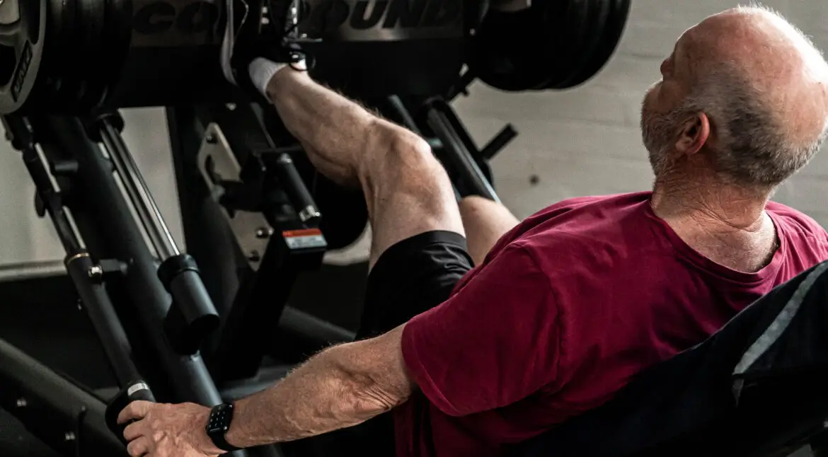Older man performing heavy leg presses on a machine in the gym, focusing on lower body strength.