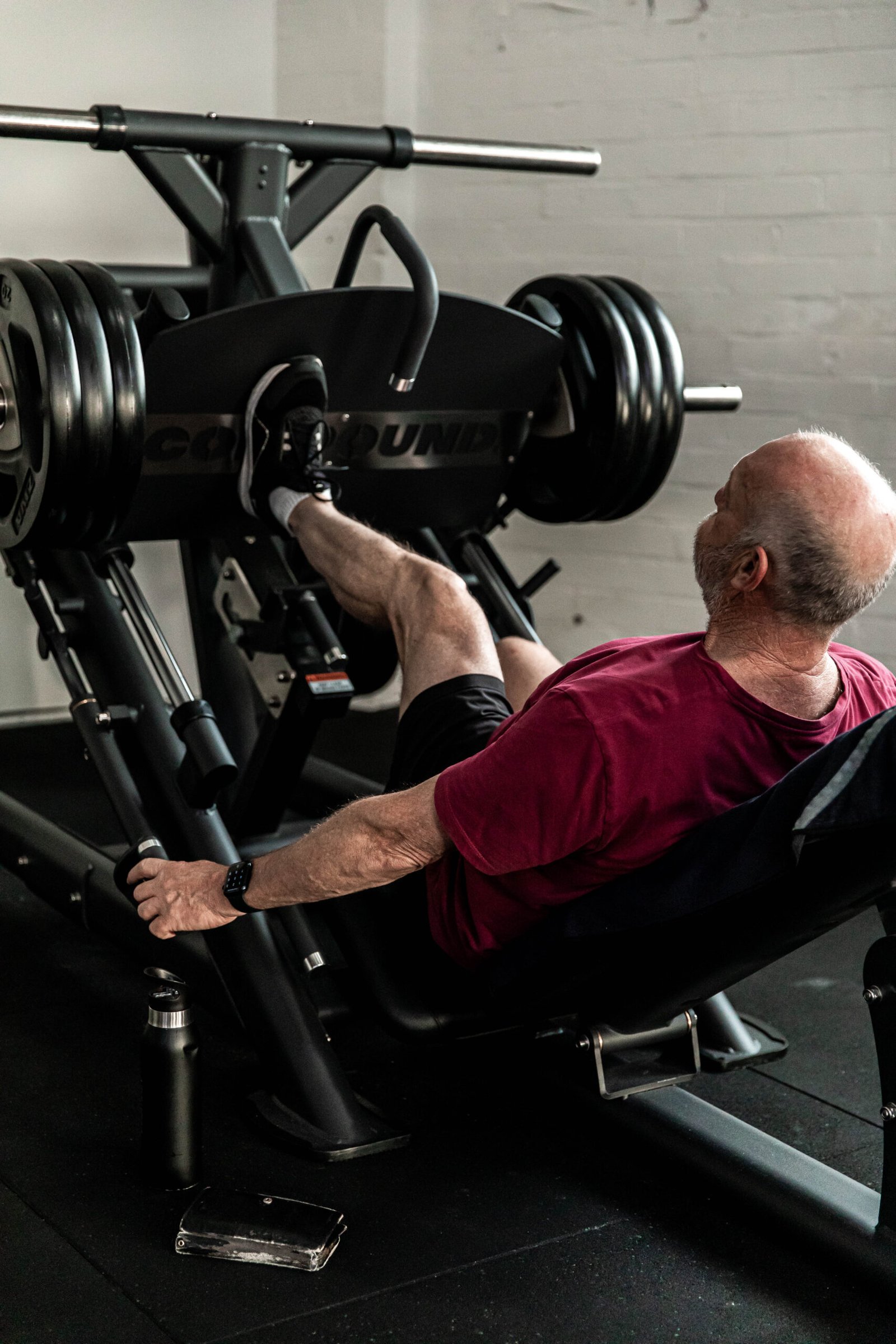 Older man performing heavy leg presses on a machine in the gym, focusing on lower body strength.