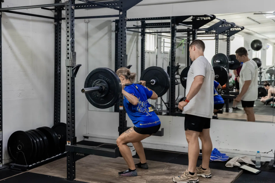 A Catalyst member back squatting with a coach spotting at Catalyst Training Co Randwick